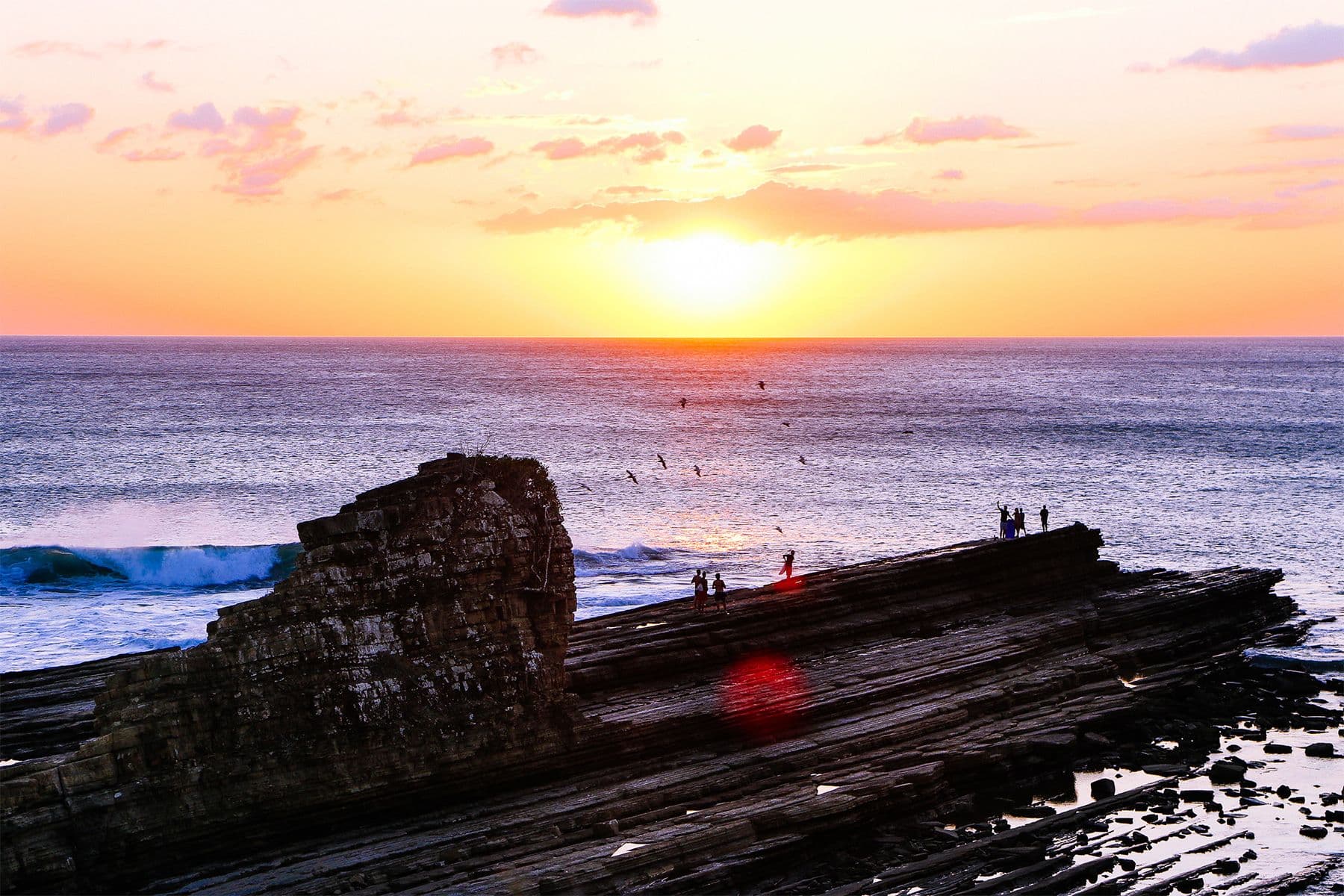people watching the sunset from rocks overlooking the pacific ocean in nicaragua